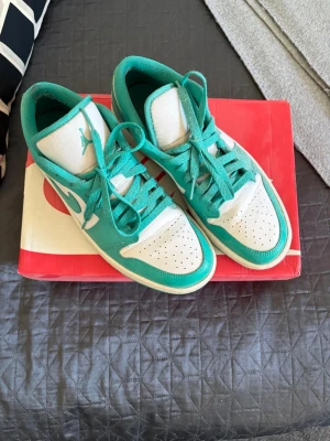 Nike Air Jordan 1 Emerald Low 42,5 - Säljer ett par Nike Air Jordan 1 Low sneakers i fräscha turkosa och vita färger. Skorna har klassisk låg siluett, perforerad tåbox och ikonisk swoosh på sidan. Ovandelen är i läder med matchande turkosa skosnören och detaljer.