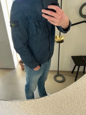Stone Island overshirt - Stone Island jacka för herr i storlek S. Jackan är blå och tillverkad i bomull. Modellen har dragkedja framtill, bröstficka med lock samt sidofickor. Ärmarna har knapp vid mudd och den klassiska Stone Island-detaljen syns på ärmen. Passar som lätt ytterjacka i vardagen. Nypris ca. 4500kr. I gott skick, hör av dig för fler bilder. 