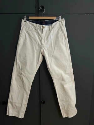 Vita chinos från Morris - Snygga vita chinos från Morris med klassisk passform och diskreta fickor fram. Byxorna har en stilig knapp i midjan och insidan är fodrad med mörkblått tyg med små vita prickar. Perfekta för en clean och stilren look. Exklusiva chinos som ger dig uppmärksamhet! 