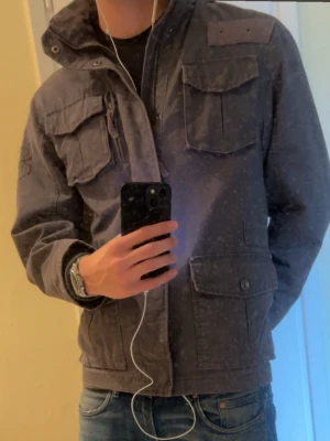Grå field jacket  - Säljer en grå parkajacka med fyra stora fickor framtill och dragkedja. Perfekt för dig som vill ha en stilren och funktionell jacka till vardags, speciellt nu mot hösten. Denna field jacket har inge defekter alls Priset är inte hugget i sten, släng iväg ett dm om du har några frågor 😁