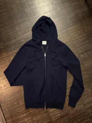 Mörkblå cashmere hoodie John Henric - Snygg mörkblå hoodie i mjuk cashmere från John Henric. Dragkedja framtill, två fickor och justerbar huva med snören. Perfekt för dig som vill ha en stilren och lyxig hoodie med skön känsla.