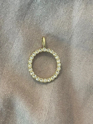 Guldigt cirkelhalsband med stenar - Snyggt halsbandshänge i form av en cirkel, tillverkat i guldfärgad metall och dekorerat med gnistrande klara stenar runt hela ringen. Perfekt för att ge din look lite extra bling och stil. Minns ej helt varifrån den är, men det är troligtvis från Guldfynd