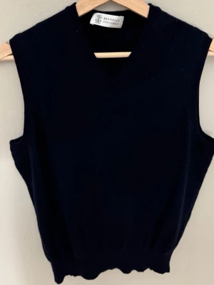Mörkblå stickad väst Brunello Cucinelli - Klassisk mörkblå stickad väst från Brunello Cucinelli med v-ringning. Perfekt att styla över en skjorta eller t-shirt för en clean och tidlös look. Mjuk och skön känsla tack vare det stickade materialet.0769