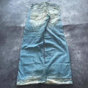 Ljusblå distressed vintagejeans för herrar i storlek W31 L34 - Stilrena ljusblå vintagejeans med en framträdande distressed-look. Bekväm passform och kvalitetsdenim. W/L är uppskattade utifrån måtten.  Mått 📏 Midja: 41 cm Benslut: 24 cm Lår: 32 cm Totallängd: 108 cm  Skickas inom ett dygn Spara på priset och frakten genom att sätta ihop ett paket Mer information finns på min profil  18-406