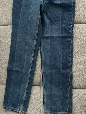  Tommy Hilfiger ”IZZY” jeans - Snygga blå jeans från Tommy Hilfiger med raka ben och klassisk femficksmodell. Jeansen har detaljer i rött och vitt vid fickorna samt logga på linningen. Tillverkade i slitstark denim med dragkedjegylf och bälteshällor.
