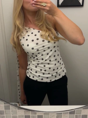 Prickig oneshoulder topp - Snygg vit oneshoulder topp med svarta prickar. Toppen är figurnära med ett knyte på axeln.