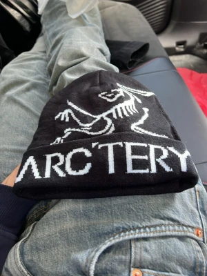 Svart Arc'teryx mössa med logga - Säljer en svart mössa från Arc'teryx med vit logga och text framtill, den är perfekt för den som vill sticka ut men inte använda skumma färger och den som har lite streetwear looken. Priset är absolut inte spikat i sten så kom med förslag!