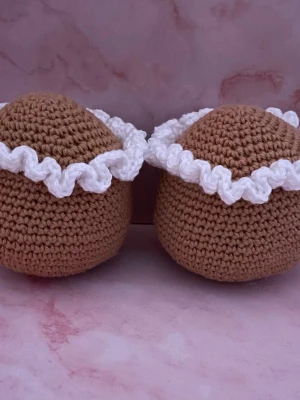 Virkade bruna semlor - Två handgjorda virkade semlor i brunt garn med dekorativ vit virkad grädde. Semlorna har en rund form och är perfekta som dekoration eller leksak. Tillverkade i mjukt garn och har en söt, lekfull design som passar alla åldrar.