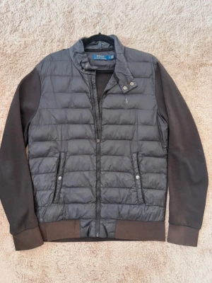 Svart cardigan jacka från Polo Ralph Lauren Storlek S - Snygg svart cardigan jacka från Polo Ralph Lauren med quiltad kropp och släta ärmar. Jackan har ståkrage med tryckknappar, dragkedja framtill och två fickor med knappstängning. Diskret logga broderad på bröstet. Perfekt för kalla vinterdagar eller på hösten eller våren. Storlek Small och är i bra skick förutom att delar på dragkedjan har lossn att. Går att justera dragkedjan fortfarande 