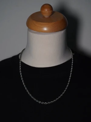 Silver Cuban Chain 4 mm – 50 cm - Snygg silverfärgad Cuban Chain i rostfritt stål ✨ Kedjan fångar ljuset riktigt fint och ger ett stilrent men samtidigt lite lyxigare look.  📏 Bredd: 4 mm 📐 Längd: 50 cm 🔩 Material: Rostfritt stål 🎁 Levereras i en svart fancy smyckespåse  Passar lika bra till vardags som när du vill klä upp dig lite extra. 🖤  Skickas välpackad! Sökord: silverfärgat halsband, smycken, silverfärgat smycke. 