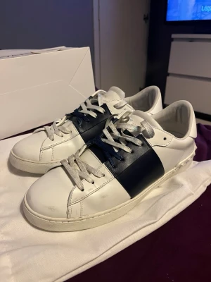 Vita sneakers med marinblå detalj - Snygga vita sneakers med märket Valentino open. Storlek 44 och passar perfekt på mig med storlek 43. Dom har lite slitage där av priset. Tillverkade i slätt läder med vit sula och diskret design som passar till det mesta.