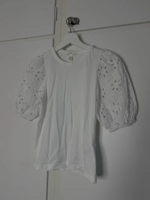 Vit topp med broderade puffärmar - Säljer en vit topp med puffiga, broderade kortärmar i blommigt mönster. ärmarna har fina hålbroderier som ger en romantisk känsla. Perfekt till jeans eller kjol för en söt look.