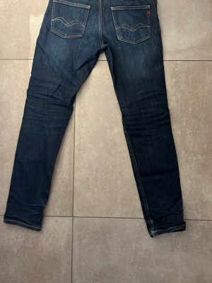 Mörkblå raka jeans med kontrastsömmar - Säljer ett par mörkblå jeans med raka ben och snygga kontrastsömmar på bakfickorna. Jeansen har klassisk femficksdesign och detaljer i gult. Perfekta för dig som gillar en enkel men stilren look.