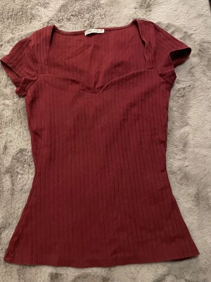 Vinröd ribbad topp från Anna Field - Snygg vinröd topp från Anna Field med ribbad struktur och v-ringad hals. Modellen är figurnära med korta ärmar. Använd 1 gång.