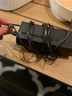 Svart nätadapter med kabel - Säljer en svart nätadapter med tillhörande kabel och rund kontakt. Adaptern har rektangulär form och är tillverkad i plast. Perfekt för dig som behöver extra strömadapter till elektronikprylar.