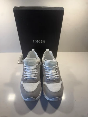 Vita och grå sneakers - Snygga sneakers från i vitt och ljusgrått med mesh och mockadetaljer. Klassisk låg modell med vita skosnören och diskret logga på plösen. Perfekta för dig som gillar stilrena och exklusiva sneakers.