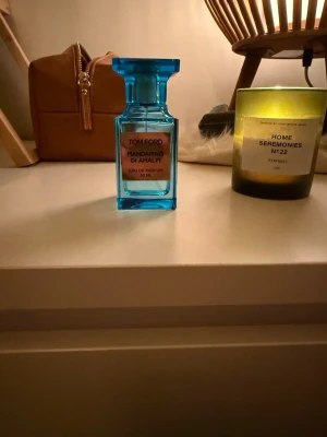 Tom Ford Mandarino di Amalfi parfym - Fräsch parfym från Tom Ford, Mandarino di Amalfi, i en snygg blå glasflaska på 50 ml. Flaskan har en elegant, fyrkantig form och sticker ut med sin klara färg och exklusiva design. Perfekt för dig som gillar lyxiga dofter och vill ha något unikt på hyllan.