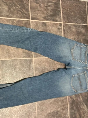 Blå slitna jeans med raka ben Tommy hilfiger SIZE 152!! - Säljer ett par blå jeans i denim med raka ben och slitna detaljer framtill. Jeansen har fem fickor, normalhög midja och ljusare partier för en trendig look. Materialet är klassisk bomullsdenim. Size 152!!