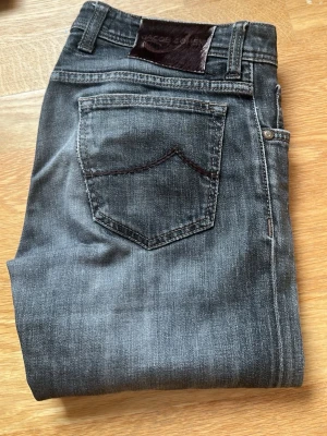 Mörkgrå jeans från Jacob Cohen - Snygga mörkgrå jeans från Jacob Cohen med klassisk femficksmodell och knappgylf. Jeansen har diskreta slitningar och kontrastsömmar som ger en cool look. Jeansen är i modell 622 Comfort, som en Nick och är i super fint skick!