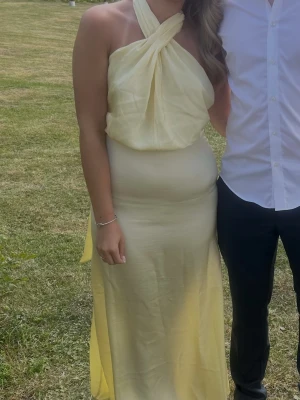 Ljusgul långklänning med halterneck - Säljer en elegant ljusgul långklänning med halterneck och draperad överdel. Klänningen har en figurnära passform och är ärmlös, perfekt för sommarens tillställningar. Endast använd en gång, nypris:1200