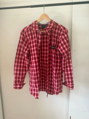 Calvin Klein skjorta - Säljer en klassisk röd och vit rutig skjorta med lång ärm och knappar framtill. Skjortan har en avslappnad passform och en liten bröstficka med diskret logga. Perfekt för dig som gillar en tidlös och avslappnad stil.