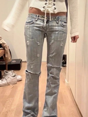 D&G jeans  - Säljer ett par ljusblå jeans med slitningar och hål på knäna. Modellen är bootcut med låg midja och klassiska fem fickor. Jeansen har en avslappnad vibe och är perfekta för en trendig streetstyle-look. hålen på baksidan är lagade så inget som syns när dem används 