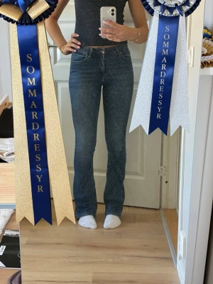 Blå bootcut jeans med hög midja - Säljer ett par klassiska blå bootcut jeans med hög midja och femficksmodell. Jeansen har en snygg tvätt och sitter tajt över låren för att sedan bli vidare nedtill. Perfekta till sneakers eller boots och ger en retrovibe till din outfit.