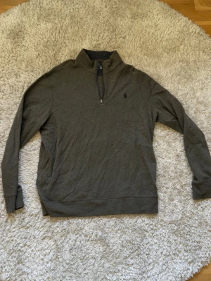 Grön halvzip från Polo Ralph Lauren - Snygg grön långärmad tröja från Polo Ralph Lauren med halvzip och liten broderad logga på bröstet. Tillverkad i mjukt bomullsmaterial och har ribbade muddar vid ärmslut och nederkant. Perfekt för en clean och avslappnad stil.
