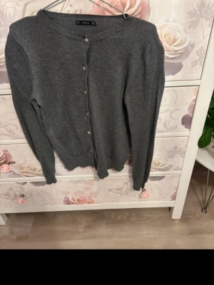 Grå kofta från ZARA Knit - Mysig grå kofta från ZARA Knit med rund halsringning och knäppning framtill. Tillverkad i mjukt stickat material och har långa ärmar. Perfekt att slänga över en t-shirt eller blus för en enkel och stilren look.