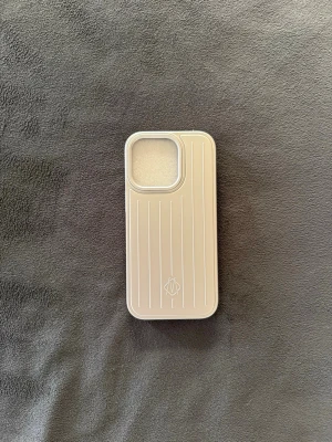 Rimowa(passar många modeller) - Snyggt beige mobilskal med räfflad yta och stilren look. Skalet har ett diskret mönster med vertikala linjer och en öppning för kameran. Tillverkat i tåligt plastmaterial som skyddar mobilen mot repor och stötar. Perfekt för dig som gillar minimalistisk stil. Byggd för iphone 16 pro men passar till vanlig o t ex 15, 17
