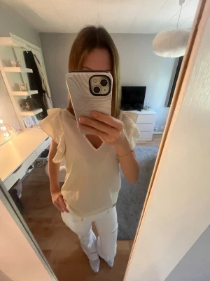 Beige blus med volangärmar och v-ringning - Säljer en söt beige blus med v-ringad hals och volangdetaljer på ärmarna. Blusen har en luftig passform och är perfekt för dig som gillar en feminin och stilren look. Materialet känns mjukt och lätt💕