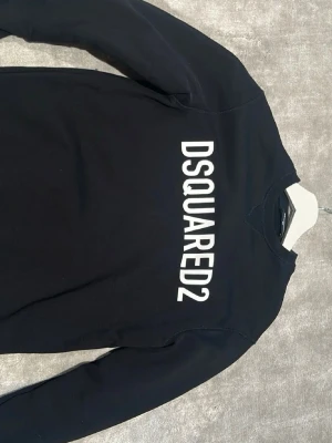Svart sweatshirt från Dsquared2 - Cool svart sweatshirt från Dsquared2 med stor vit logga tryckt över bröstet. Tröjan har rund halsringning och långa ärmar. Perfekt för en avslappnad och trendig look.