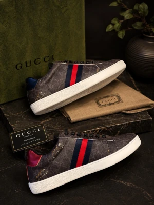 Gucci ace tiger - Snygga sneakers från Gucci i mörkbrunt med klassiskt GG-mönster och gulddetaljer. Skorna har vita sulor, svarta skosnören och de ikoniska röd/blå ränderna på sidan. Baktill finns en kontrastfärg i rött och blått. Materialet är canvas och läder.