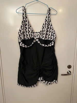Svartvit tankini med zigzag-mönster, utan underdel , stl XL  - Snygg tankini i svart och vit. Djup urringning och dekorativ knytning framtill. Materialet är stretchigt och bekvämt, perfekt för stranden eller poolen. Stl XL