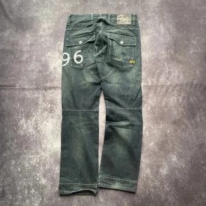G-Star Raw 96 vintagejeans för herrar i mörkblått, storlek W33 L32 - Midja: 44 cmBenslut: 21 cmLår: 32 cmTotallängd: 107 cmSkickas inom ett dygnSpara på priset och frakten genom att sätta ihop ett paketMer information finns på min profil10-257