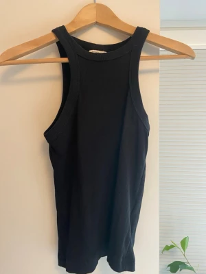 Svart ribbad linnetopp Gina Tricot - Säljer en svart ribbad linnetopp från Gina Tricot, modellen basically basics. Toppen är ärmlös med breda axelband och har en tight passform. Perfekt att styla till jeans eller kjol för en clean och enkel look.