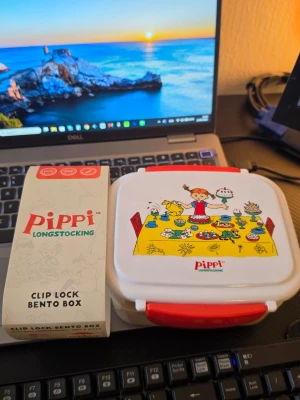 Pippi Långstrump matlåda och vattenflaska - Säljer en vit och röd matlåda med Pippi Långstrump-motiv och texten 'Pippi Longstocking', samt en rosa vattenflaska med pop art-inspirerat motiv. Perfekt för skolan eller utflykten. Matlådan har clip lock och vattenflaskan har praktiskt lock.