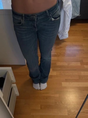 Blå jeans med låg midja - Säljer ett par klassiska blå bootcut jeans med låg midja. Jeansen har fem fickor och stängs med dragkedja och knapp. Materialet är denim i bomull och de har en avslappnad passform som passar till många olika stilar.