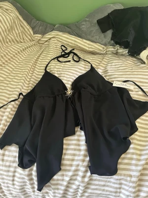 Svart linnetopp  - Säljer en svart linnetopp från New Collection. Toppen har tunna knytband i nacken och vid ryggen och en solformad brosch💕 Storlek står inte men skulle säga S