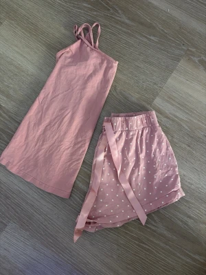 Rosa pyjamasset med linne och shorts - Sött pyjamasset i ljusrosa med ett linne med smala axelband och matchande shorts med vita prickar och sidenband i midjan. Båda I storlek xs, rena och hela.