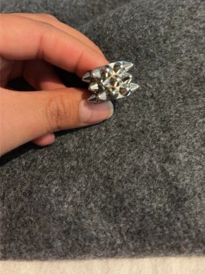 Silvrig ring med nitar från Edblad  - Cool bred ring i silverfärgad metall med flera små, spetsiga nitar på ovansidan. Ringen har en chunky design och ger ett edgy intryck. Perfekt för dig som gillar statement-smycken och vill sticka ut.
