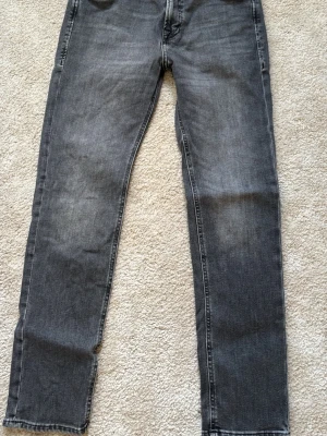 Grå raka jeans med fem fickor - Snygga grå jeans med rak passform och klassisk femficksdesign. Jeansen har subtila slitningar och kontrastsömmar. Tillverkade i ett mjukt denimtyg som ger en avslappnad look. Perfekta för dig som gillar en enkel och stilren stil.