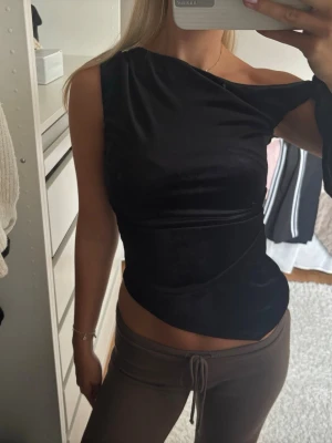 Svart oneshoulder topp i sammet - Snygg svart oneshoulder topp i mjuk sammet med asymmetrisk skärning. Toppen har en unik axelbandslös design på ena sidan och sitter tight för en smickrande siluett. Perfekt för dig som vill sticka ut med en trendig och elegant look.