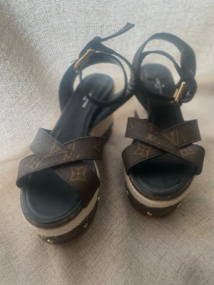 Helt oanvända Louis Vuitton kilklackar/espadrillos i klassisk Monogram-canvas - Helt oanvända Louis Vuitton kilklackar/espadrillos i klassisk Monogram-canvas. Endast förvarade i garderoben. Storlek & Passform: Stämplade 38, men upplevs som en storlek 36 då modellen är mycket liten i storleken. Innermåttet är ca 23,5 cm (se bild).Detaljer: Tillverkade i Italien. Produktionskod SA1129 finns stämplad på insidan av remmen. Säljes i befintligt nyskick utan tillbehör då de köptes secondhand i Stockholm för några år sedan. Skickas spårbart."*