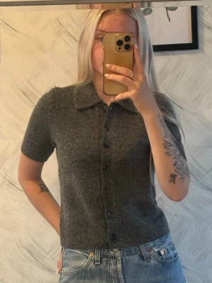 Grå kortärmad kofta med knappar - Mysig grå kofta med korta ärmar och knappar hela vägen framtill. Koftan har en klassisk krage och är stickad i ett mjukt material som ger en avslappnad men ändå stilren look. Aldrig använd.