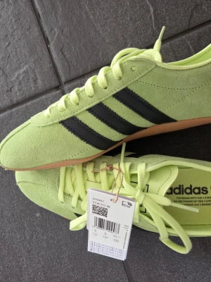 Adidas limegröna sneakers - Säljer ett par limegröna Adidas sneakers i mocka med klassiska svarta ränder på sidan och gummisula. Helt oanvända. Storlek 39 1/3. Nypris 1200 kr