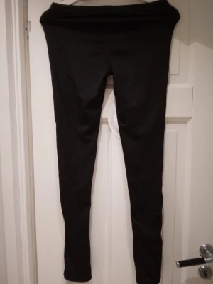 Svarta glansiga leggings från Lamote, strlk S-M - Svarta glansiga  leggings från Lavoie i storlek M/38-40, passar dock troligen även någon med Small. De har en klassisk, tight passform och hög midja. Perfekta att matcha med oversized tröjor eller hoodies. Materialet är stretchigt och mjukt för extra komfort.