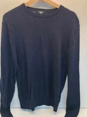 Mörkblå stickad tröja från UNIQLO - En enkel och stilren mörkblå stickad tröja med rund halsringning och långa ärmar. Tröjan har ribbade muddar vid ärmslut och nederkant. Perfekt för lager på lager och passar till det mesta i garderoben.