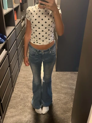 Blå bootcut jeans med kontrastsömmar - Säljer ett par ljusblå bootcut jeans med låg midja och vita kontrastsömmar. Jeansen har klassiska fem fickor och en snygg tvättad look. Perfekta för dig som gillar retrostil och vill ha ett par jeans som sticker ut lite extra.