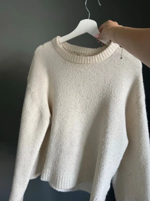 Krämvit stickad tröja från Gina - Mysig krämvit stickad tröja med rund halsringning och ribbade muddar vid ärmslut och nederkant. Tröjan har en avslappnad passform och är perfekt för kyligare dagar. Materialet är mjukt och fluffigt, vilket ger en skön känsla. Xs men är lite mer åt det oversized hållet